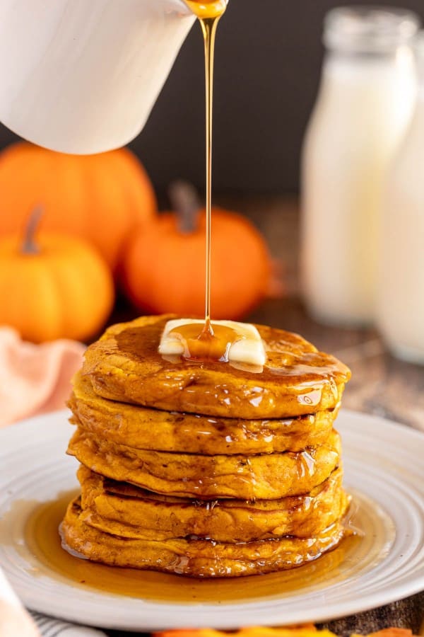 Pumpkin spice pancakes being drizzled with maple syrup.