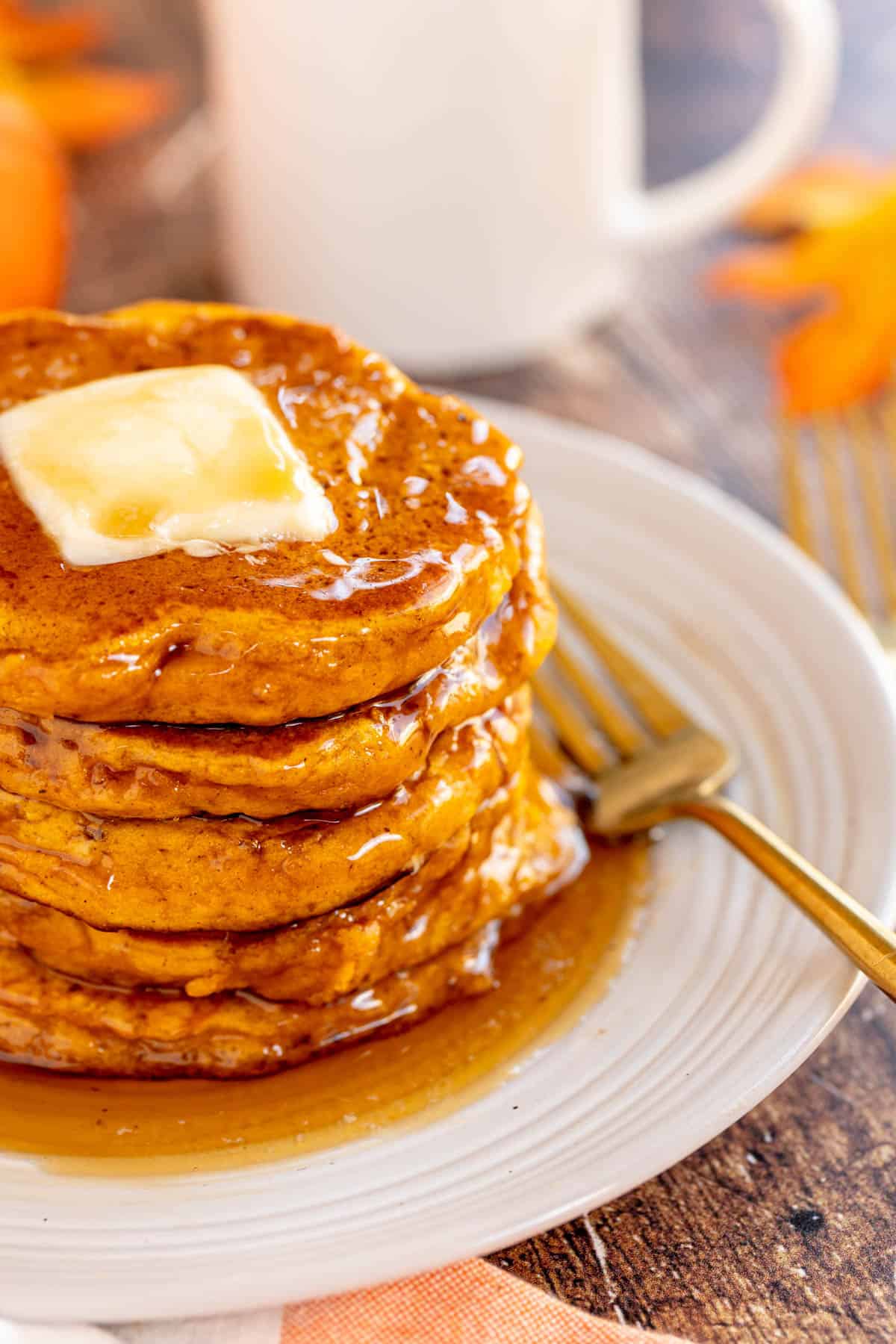 A stack of pumpkin spice pancakes with butter and syrup on a plate.