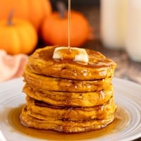Pumpkin spice pancakes being drizzled with maple syrup.