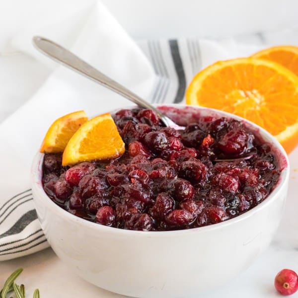 cranberry sauce in a white bowl with orange slices and rosemary