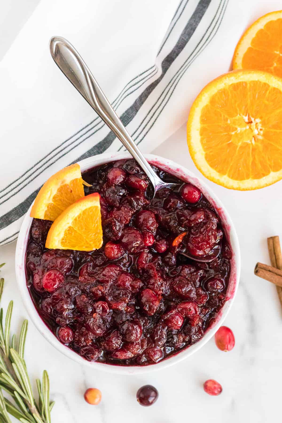 cranberry sauce in a white bowl with orange slices and rosemary
