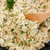 Creamy garlic parmesan risotto garnished with herbs in a black pan with a wooden spoon.