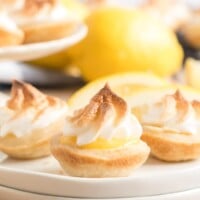 mini lemon meringue pies on a white plate with a lemon