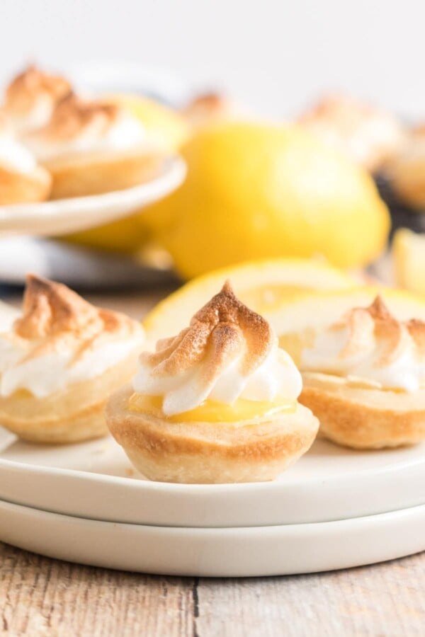 mini lemon meringue pies on a white plate with a lemon