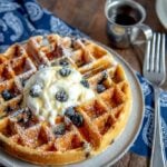 blueberry waffles with whipped cream, powdered sugar, with a fork and maple syrup.