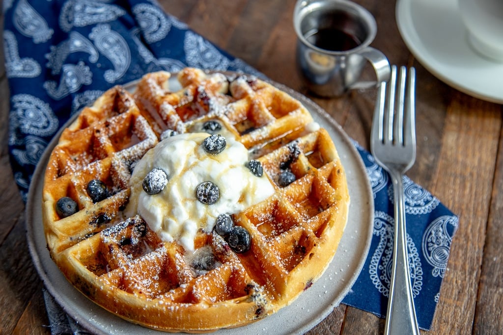 blueberry waffles with whipped cream, powdered sugar, with a fork and maple syrup