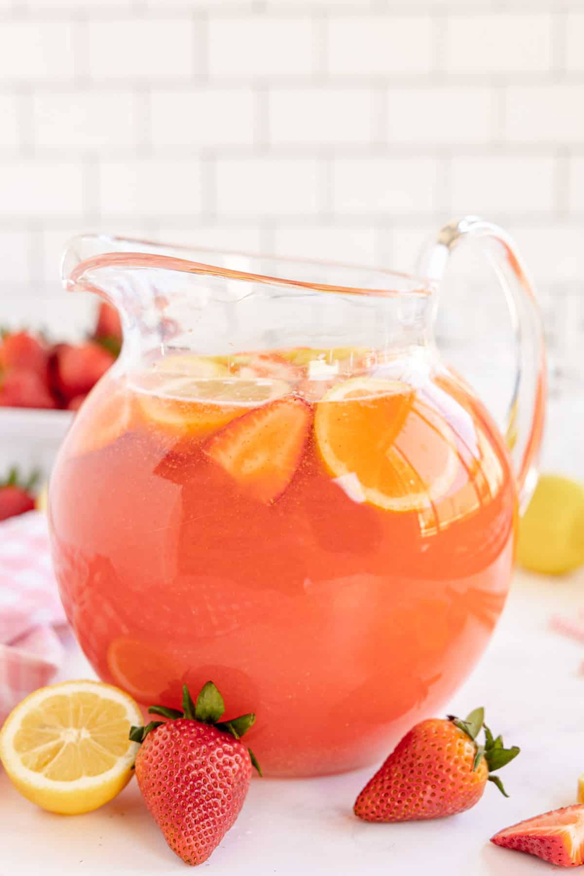 A pitcher of homemade strawberry lemonade with lemon slices and strawberries.