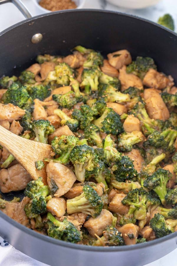 chicken broccoli stir fry in a wok with a wooden spoon.