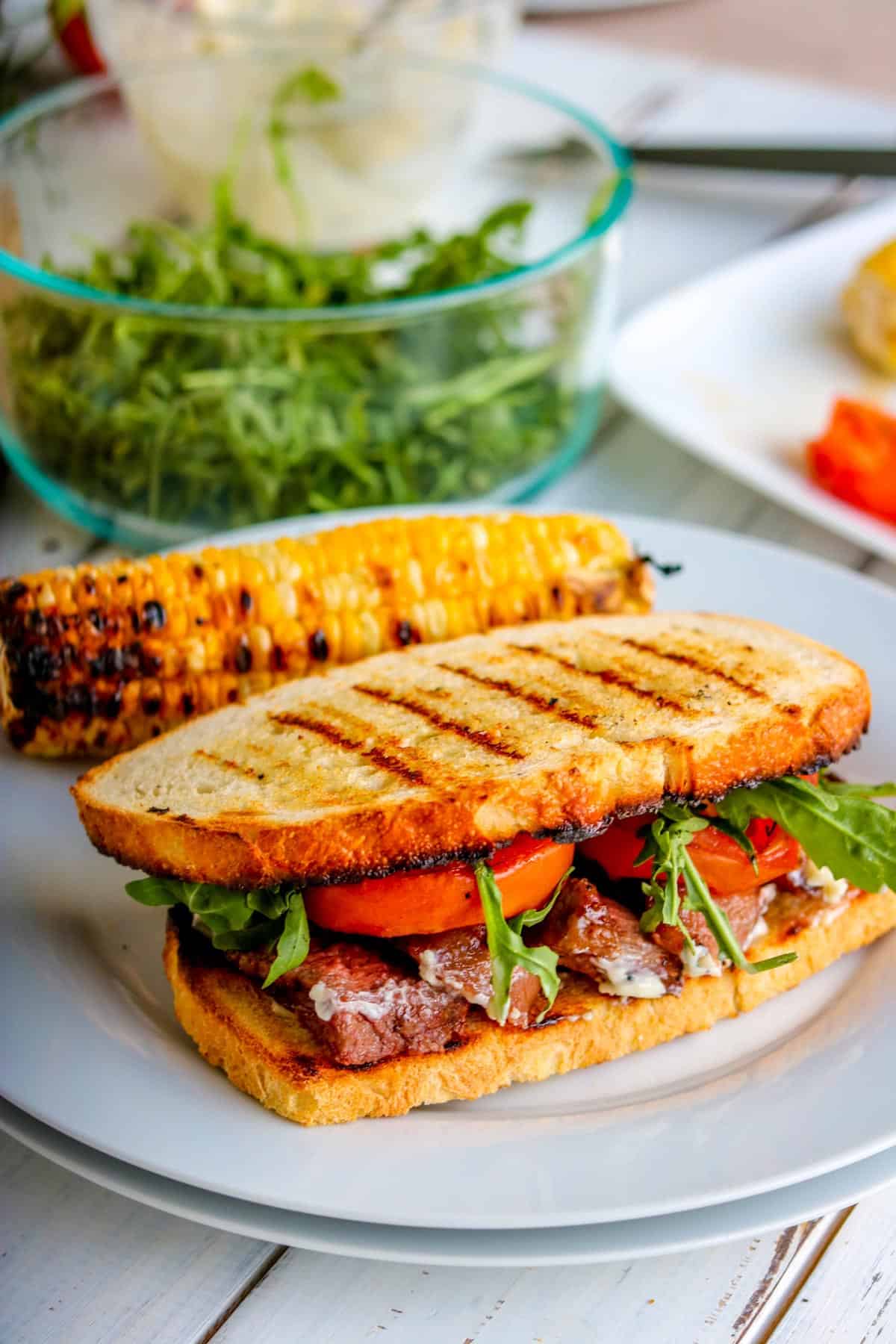 a steak sandwich with grilled bread on a white plate.