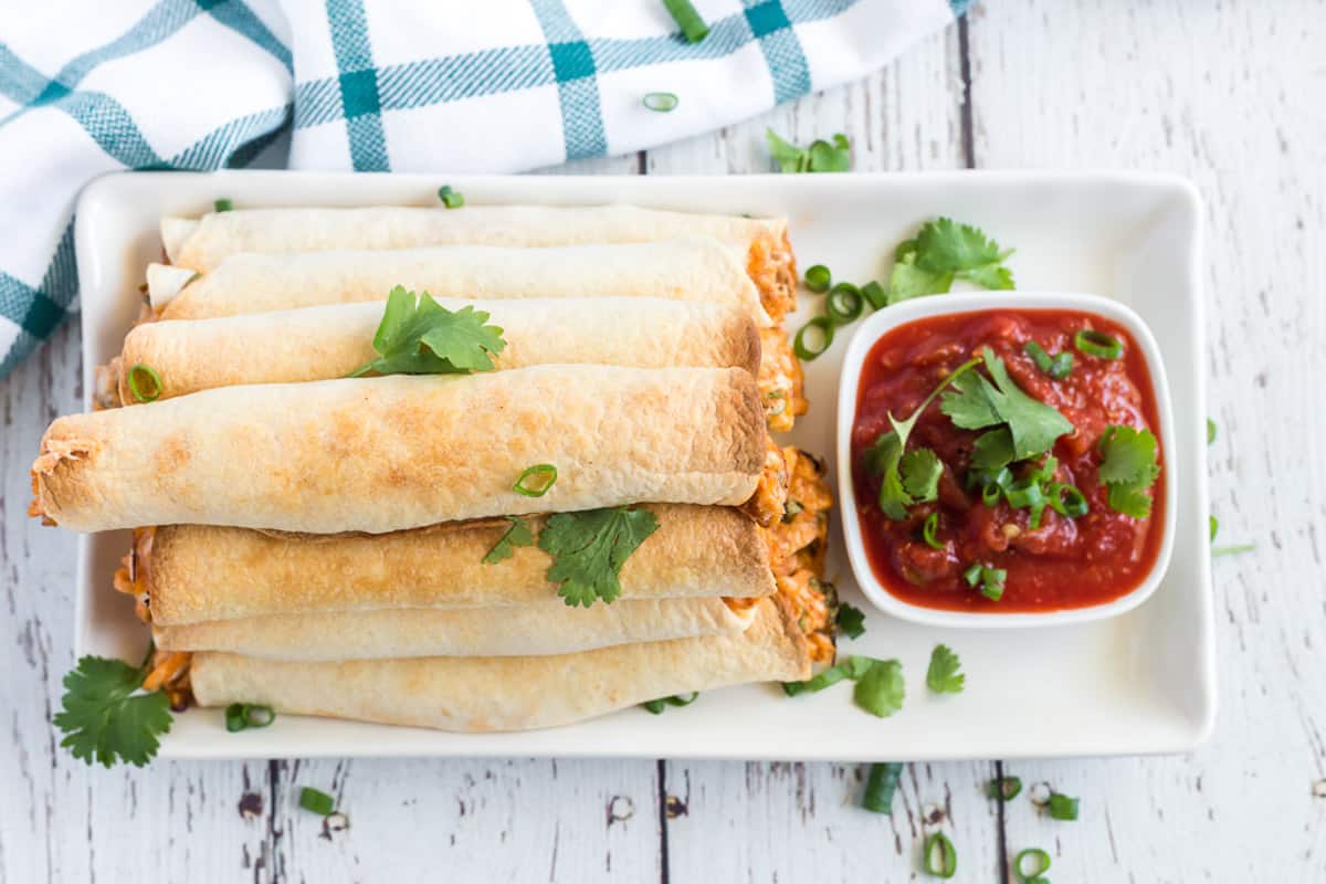 chicken taquitos on a platter with salsa.