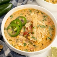 Bowl of creamy chicken tortilla soup with tortilla chips and jalapenos and limes.