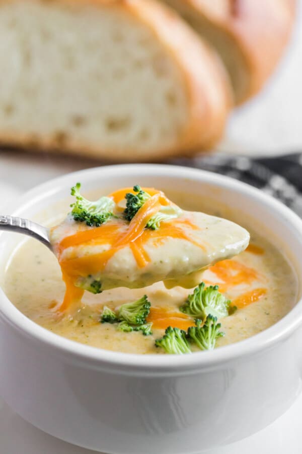 broccoli cheddar soup with a spoon out of the soup and bread in the background