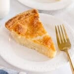 A slice of buttermilk pie on a white plate with a gold fork.