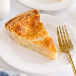 A slice of buttermilk pie on a white plate with a gold fork.