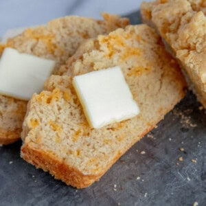 A slice of crumbly beer bread with a pat of butter on a slate surface.