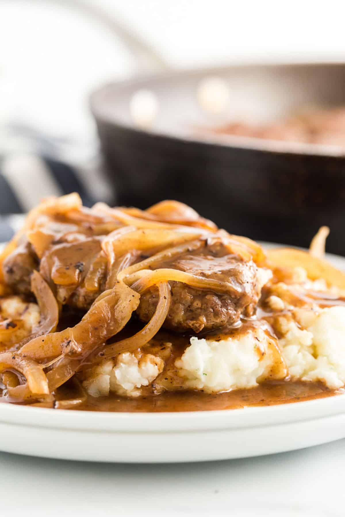 hamburger steaks with onion gravy over mashed potatoes on a white plate