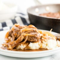 hamburger steaks on a white plate smothered in onions