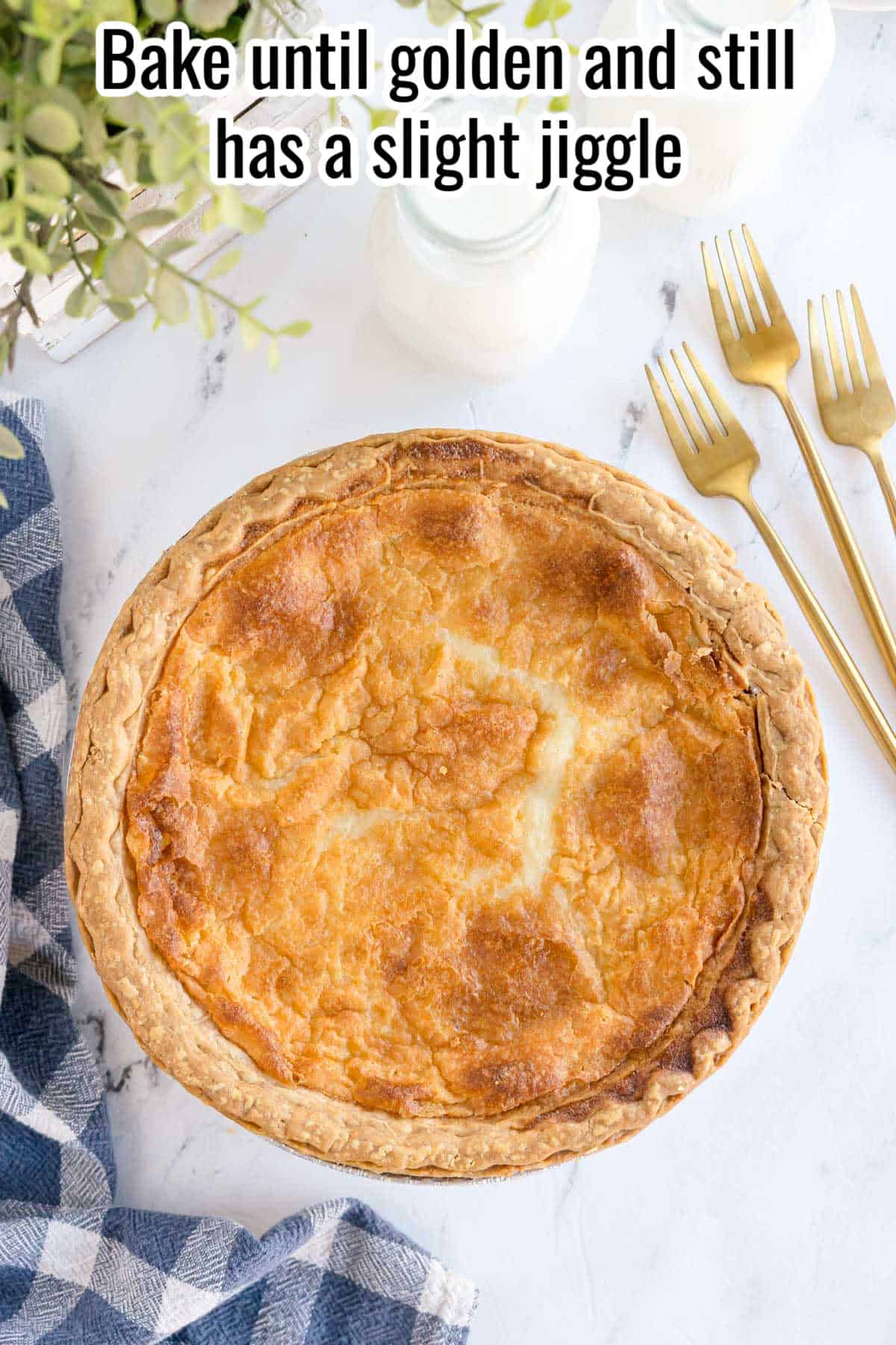 A golden-brown buttermilk pie on a white surface, with text reading “Bake until golden and still has a slight jiggle.”