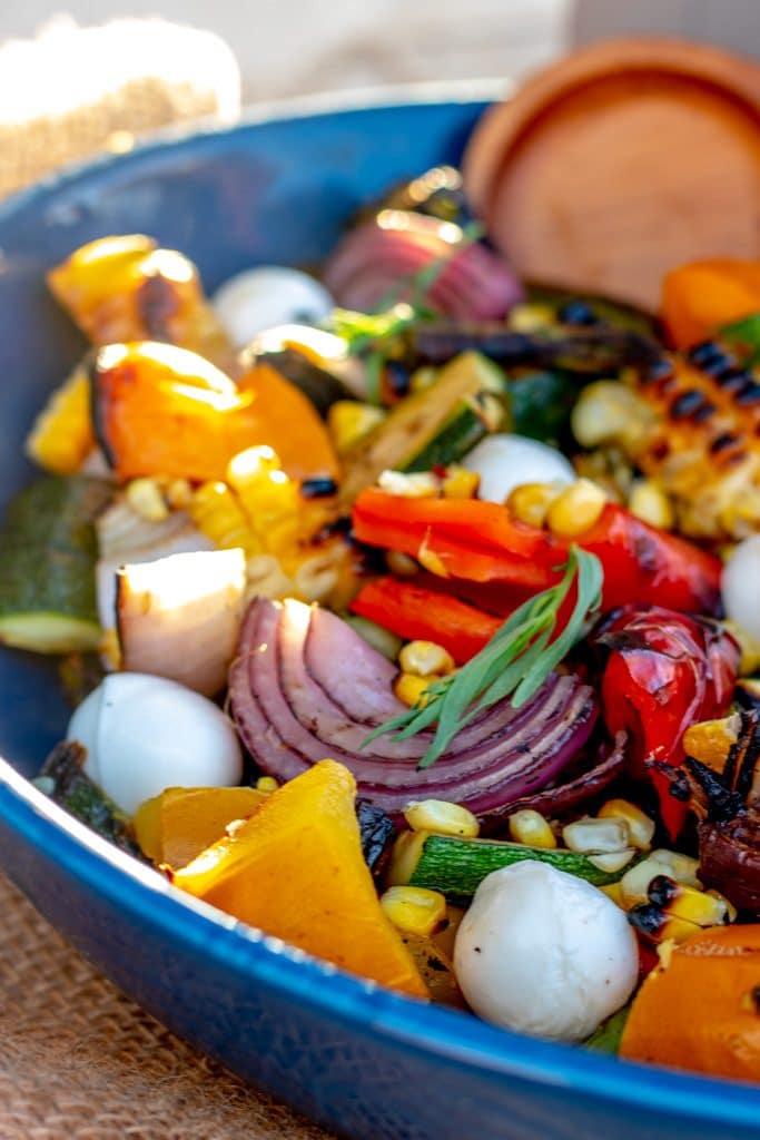 grilled vegetable salad in a blue bowl with wooden utensils