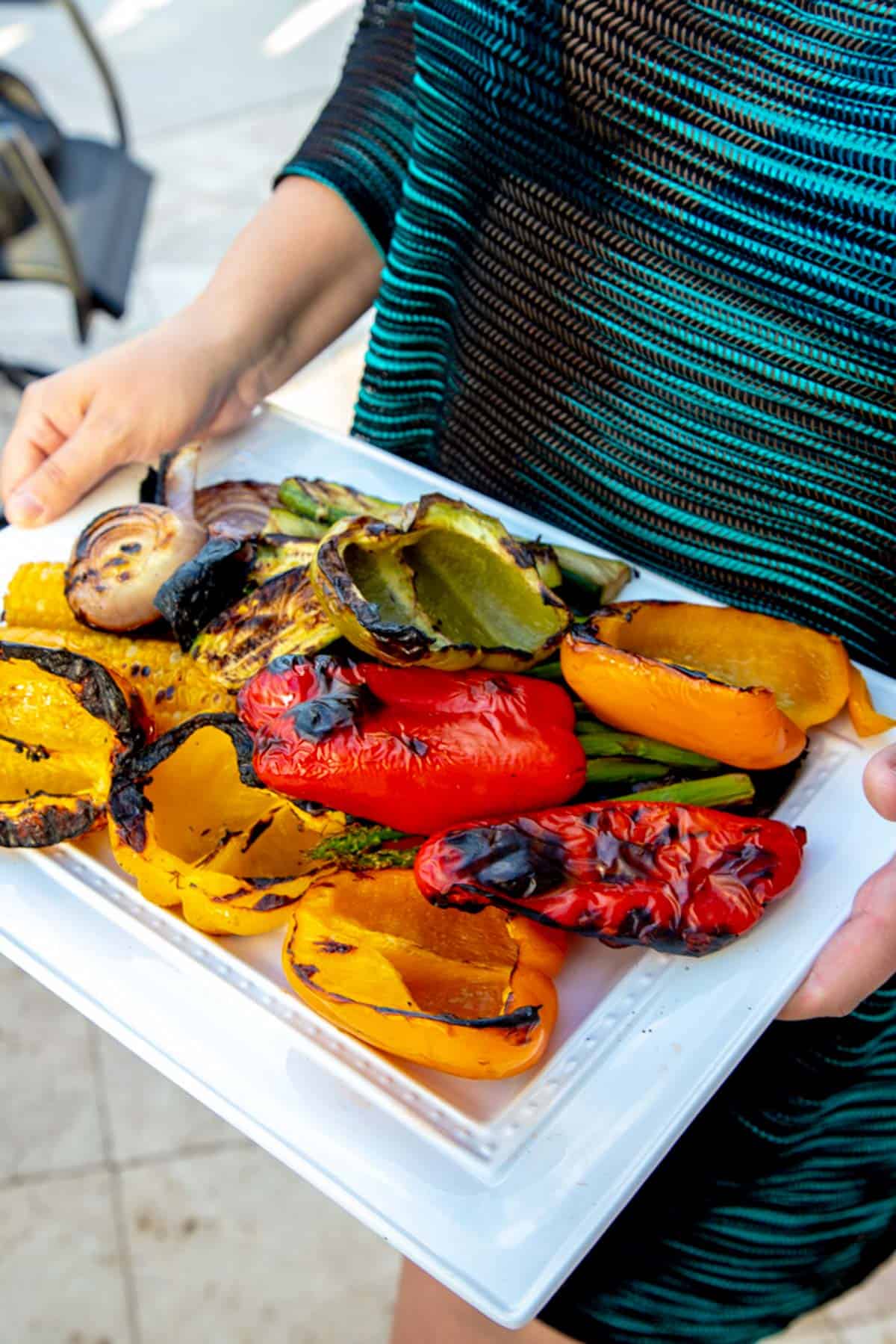 freshly grilled vegetables on a white platter being held by hands.