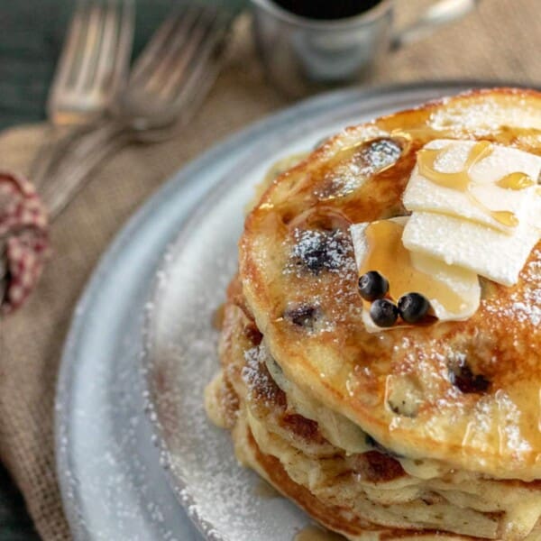 blueberry pancakes on a grey plate with forks and syrup