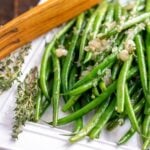 sauteed green beans on a white platter with wooden tongs