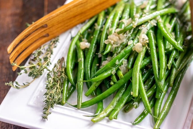 sauteed green beans on a white platter with wooden tongs