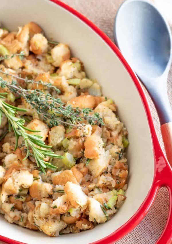 homemade stuffing in a red casserole dish with fresh herbs.