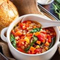 vegetable barley soup in a white bowl with a bread roll.
