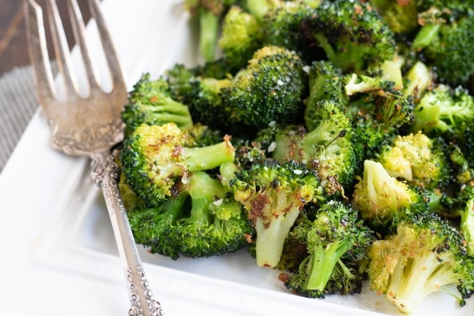 oven roasted broccoli one a white platter with an antique fork