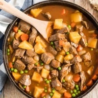stove top beef stew in a skillet with a wooden spoon.