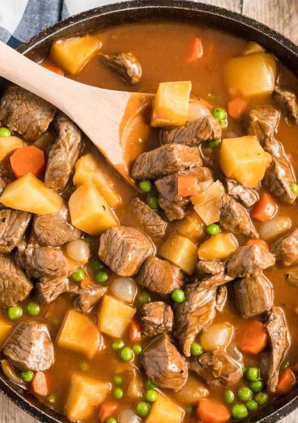 stove top beef stew in a skillet with a wooden spoon.