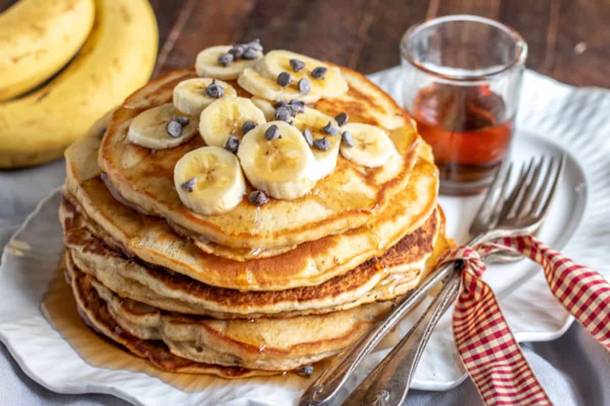 banana pancakes on a plate with syrup and silverware tied with a ribbon