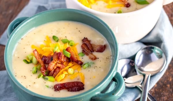 loaded baked potato soup in a teal bowl with spoons
