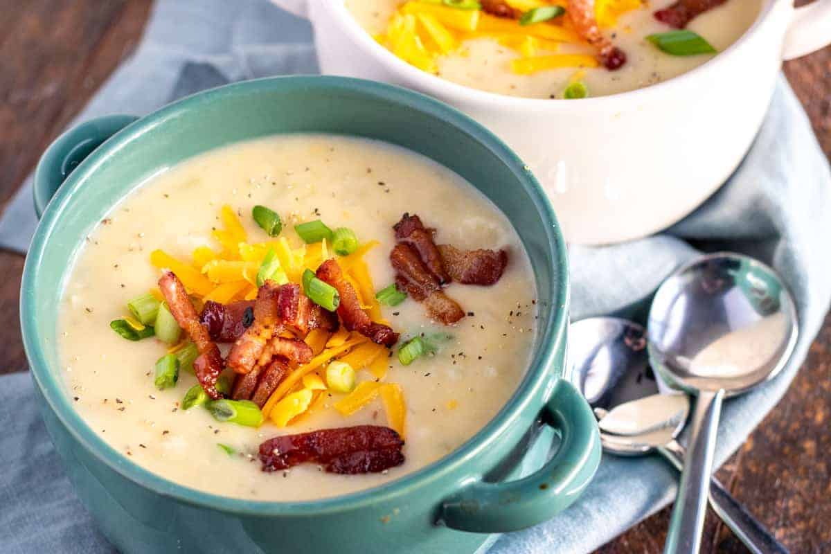 loaded baked potato soup in a teal bowl with spoons