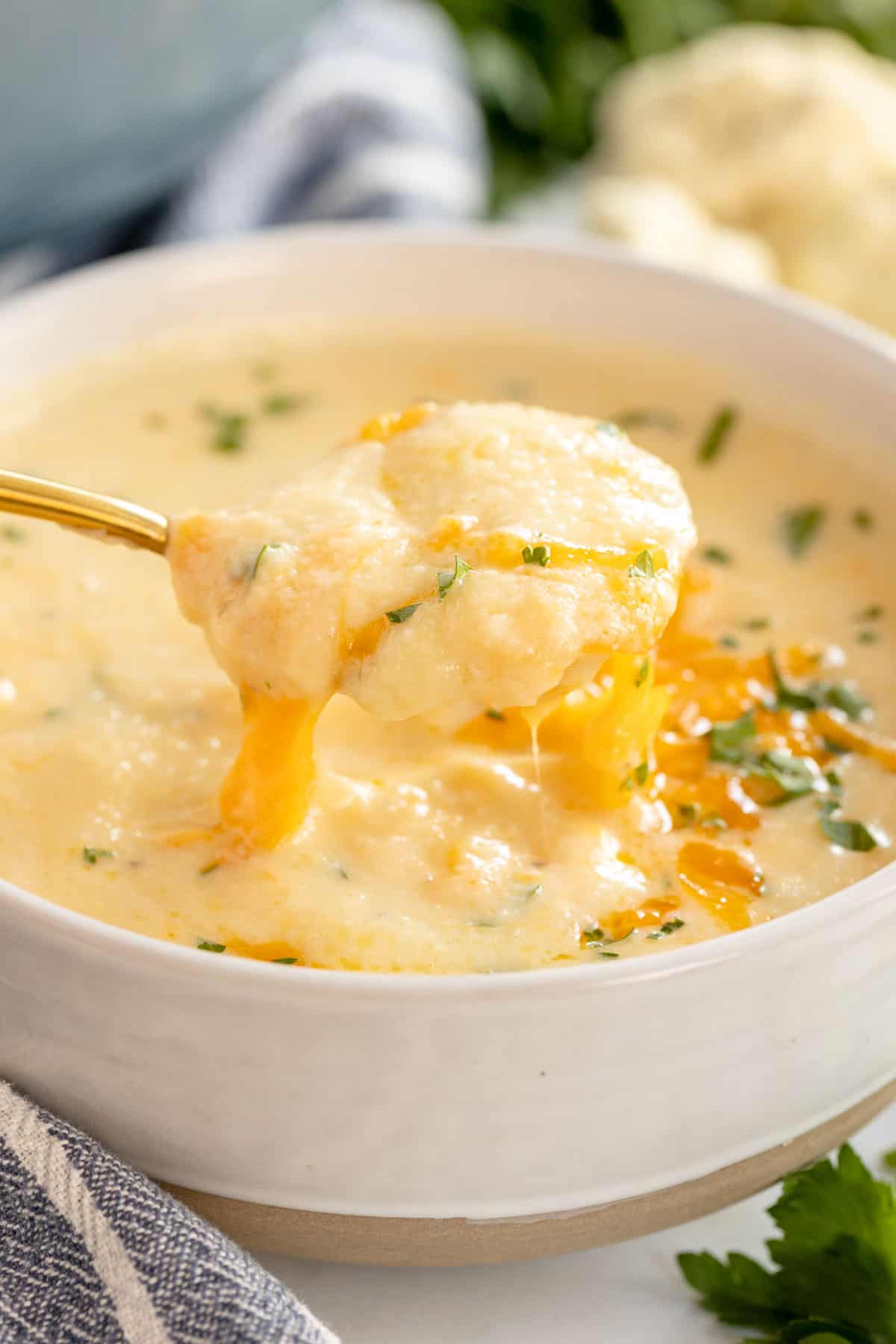 Cauliflower cheese soup in a white bowl with a spoon.