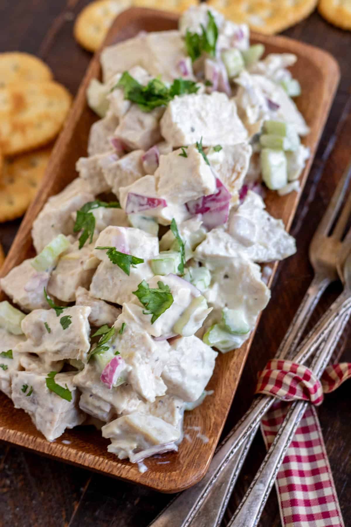 chicken salad on a wooden platter with crackers and forks.