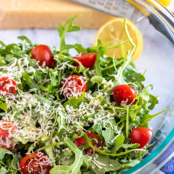 arugula salad in a bowl with lemon on the side