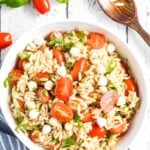 Caprese Orzo Salad in a white bowl with basil and tomatoes scattered around