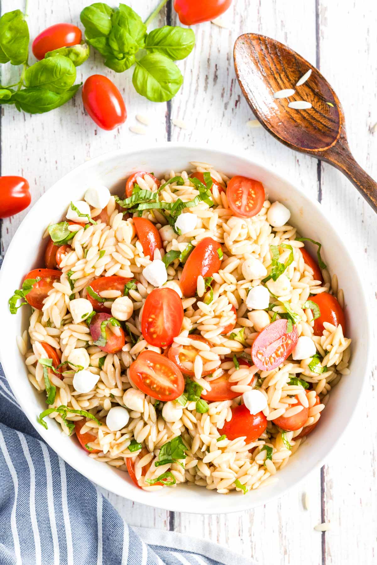 Caprese Orzo Salad in a white bowl with basil and tomatoes scattered around