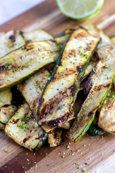 grilled zucchini on a chopping board with a lime