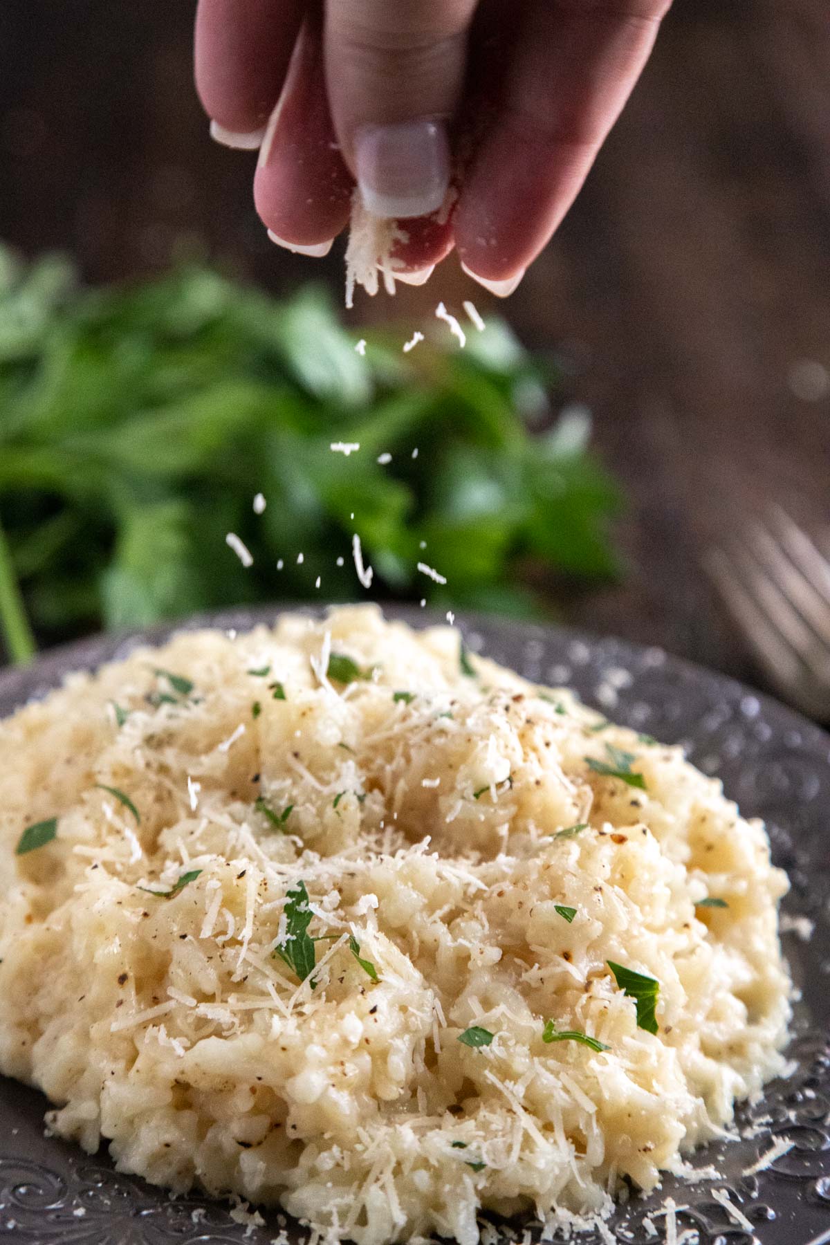 instant pot risotto with parsley in the background, a hand sprinkling parmesan cheese