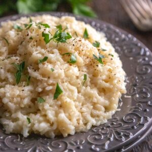 square photo of risotto on a grey plate, sprinkled with parsley