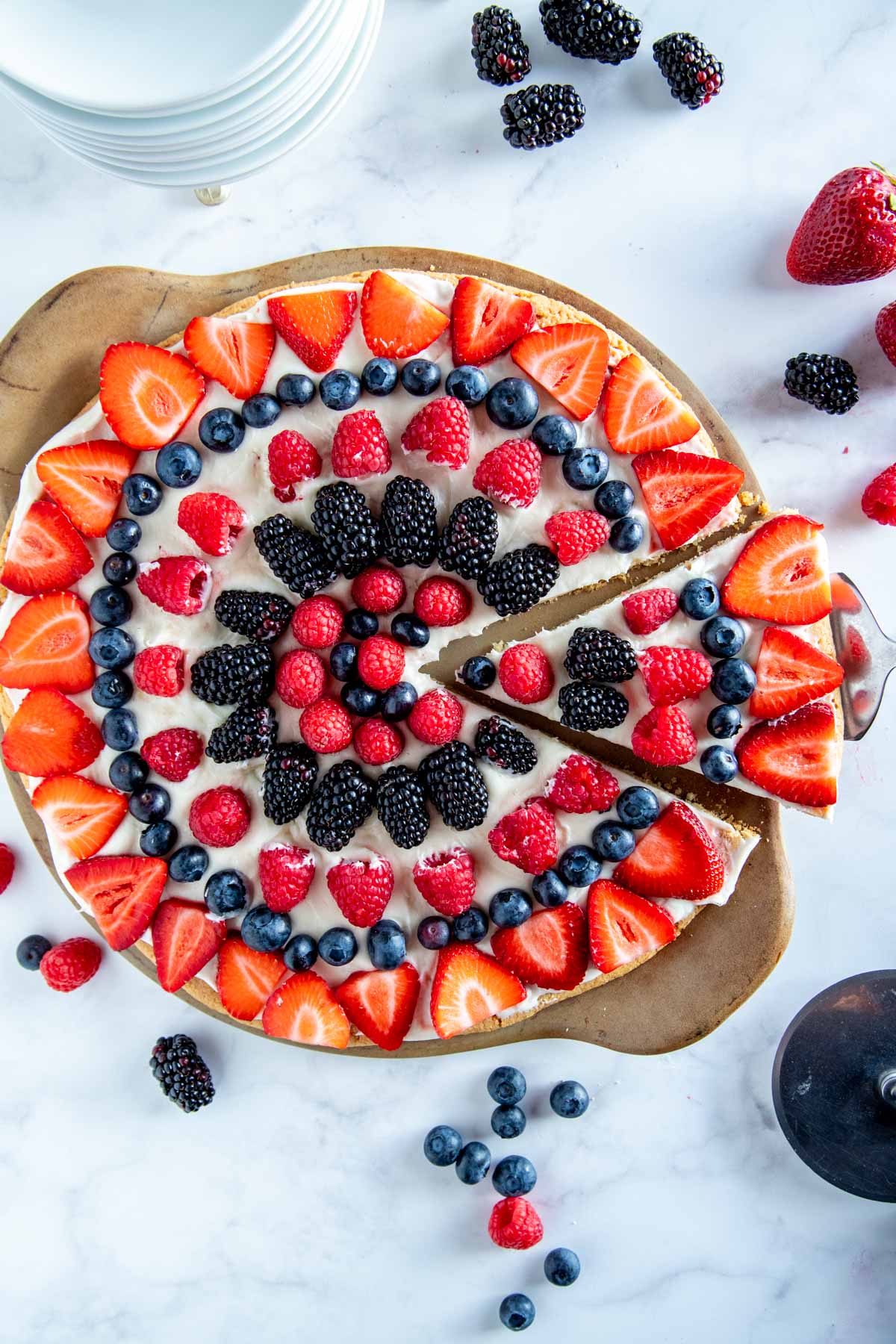 fruit pizza on a pizza stone, with berries around it