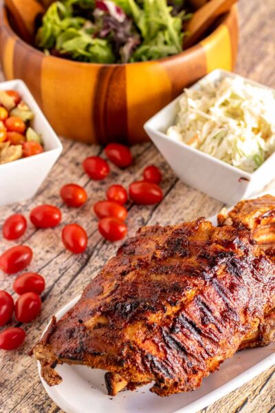 grilled ribs on a white plate with salads around