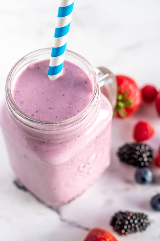mixed berry smoothie in a mason jar glass with a blue striped straw