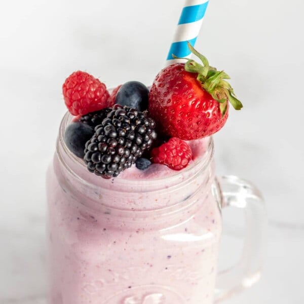 Mixed berry smoothie in a clear glass with fruit and a striped straw