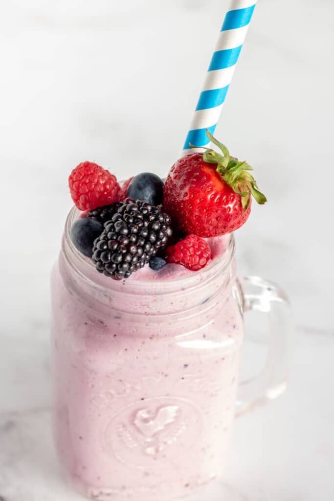 Mixed berry smoothie in a clear glass with fruit and a striped straw
