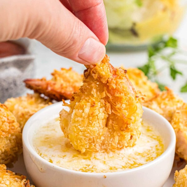hand dipping shrimp into a sauce