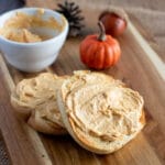 square image of a wooden board with a bagel schmeared with pumpkin cream cheese